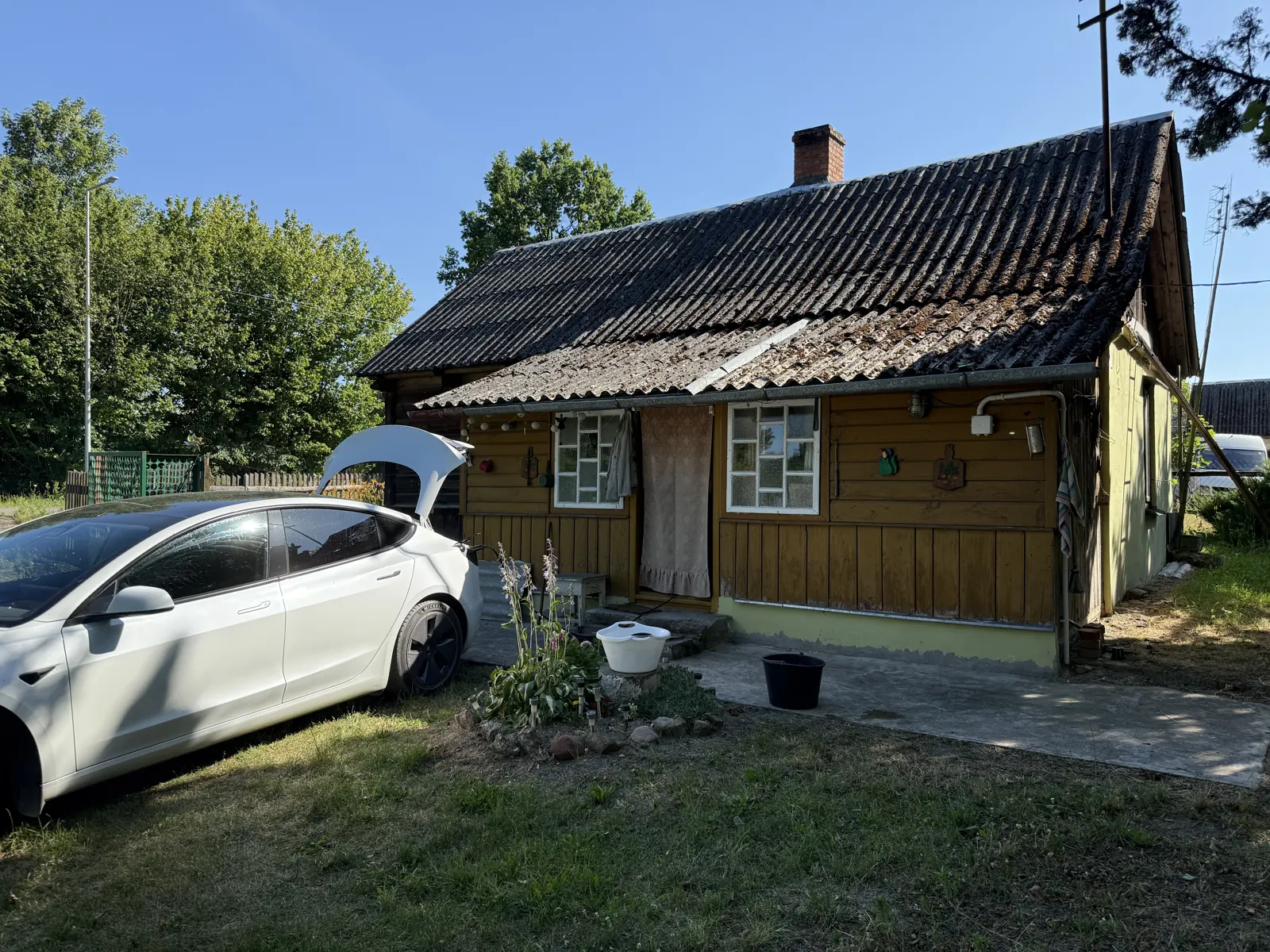 Stara chata w OAZEN, przed nią zaparkowana Tesla